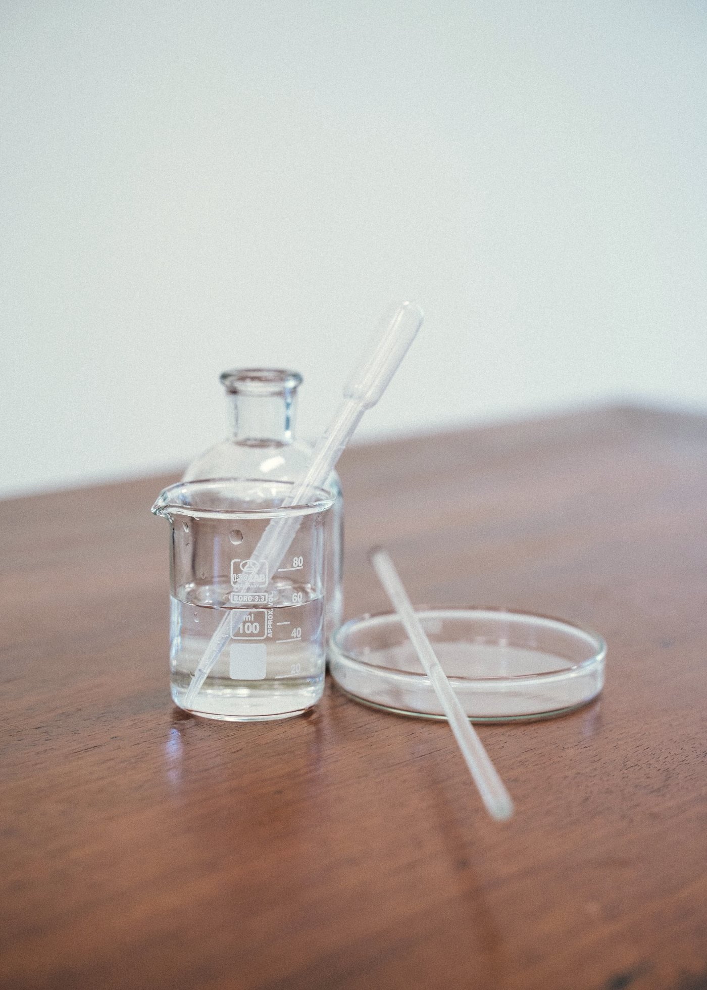 A glass beaker, stirring rod, and petri dish arranged on a wooden laboratory bench