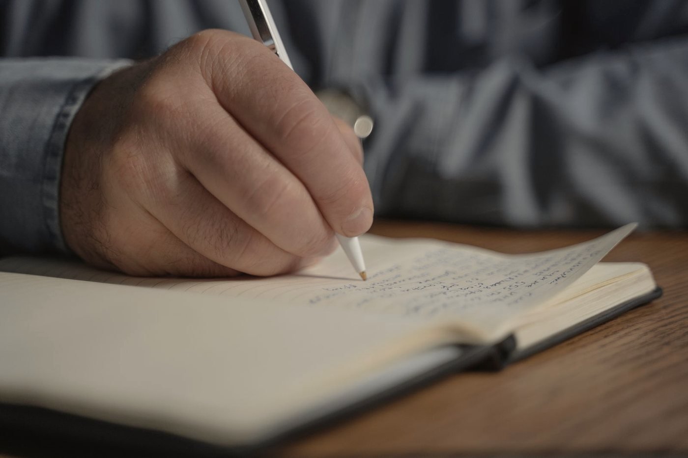 A hand writing dated entries into a bound research notebook